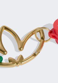 Sleutelhanger van metaal met goudkleurige afwerking in de vorm van een bloem, met een rode ronde accent en een groen stoffen lint bevestigd aan de onderkant.