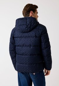 Donkerblauwe pufferjas met capuchon, voorzien van een subtiel geometrisch patroon, doorgestikt ontwerp en elastische manchetten. Achteraanzicht toont een gladde afwerking.