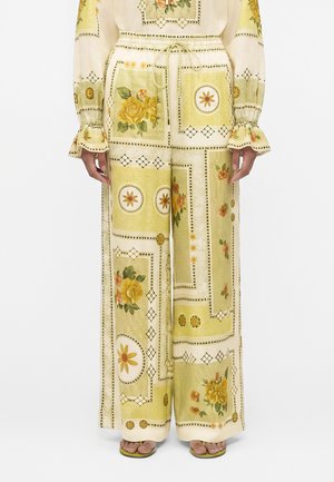 Kremowe spodnie o szerokich nogawkach z żółto-pomarańczowym kwiatowym i geometrycznym nadrukiem typu patchwork, zestawione z dopasowaną bluzką z długim rękawem i falbankowymi mankietami.