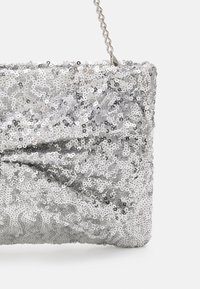 Pochette argentée ornée de sequins avec une surface douce et texturée, présentant un design torsadé et une sangle chaîne argentée.