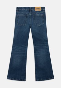 Razširjene kavbojke iz denima v temno modrem odtenku, z obliko žepe pri hrbtu in bež usnjeno oznako na pasu. Gladka tekstura.