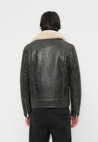 Jachetă din piele neagră cu un finisaj texturat, guler din blană și manșoane cu fermoar. Design elegant, croială ajustată și accente minimaliste.