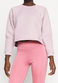 Sweat-shirt court rose clair avec un design côtelé texturé sur les manches et un petit logo Nike au centre. Associé à des leggings roses assortis.