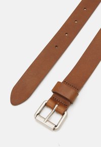 Smeđi kožni remen s glatkom teksturom, sa više rupica i srebrnom metalnom kopčom. Kraj je sužen za elegantan završetak.
