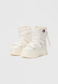Baskets montantes en tissu blanc avec des semelles épaisses et texturées ; dotées de sangles enveloppantes et d'un patch logo sur le côté.