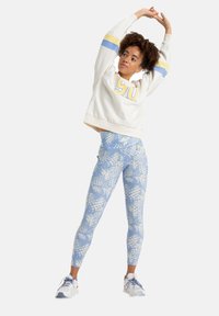 Felpa bianca corta con strisce gialle e blu, abbinata a leggings azzurri chiari con motivo ananas. Le scarpe da ginnastica completano il look.