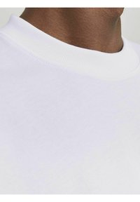 T-shirt bianca in cotone con scollatura a girocollo ribattuta, texture liscia e dettagli di cucitura minimi vicino al colletto e all'area delle spalle.