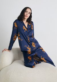 Marine satin pysj sæt med orange tiger mønstre, lange ærmer, knap-ned design og afslappet pasform, fremhævet med stjernesymboler.