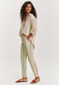 Pruhovaný voľnočasový set v pastelových farbách (ružová, zelená, žltá). Voľnejší trikoto s rukávmi na vyhrňovanie, nohavice s viazaním a ploché sandále.