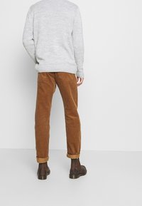 Grijze gebreide trui met geribbelde boorden, gecombineerd met brown corduroy broek met opgerolde zoom. Zwarte enkel laarzen maken de outfit compleet.