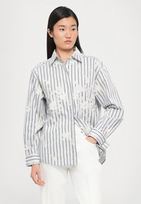 Chemise à rayures en tissu léger, avec broderies florales et col. Manches longues avec poignets boutonnés.