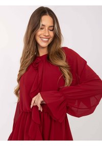 Czerwona, zwiewna sukienka z długimi, bufkami rękawami, kokardką przy dekolcie i warstwowymi falbanami na spódnicy. Przezroczysta tekstura z miękkim wykończeniem.