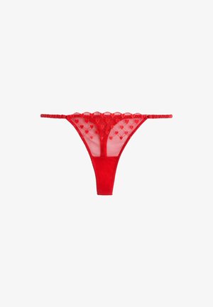 Chiloți tip tanga din dantelă roșie, cu broderie în formă de inimă, material mesh transparent și bretele subțiri reglabile în talie pe fundal alb.