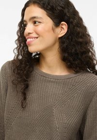 Un pull en tricot marron avec un col rond, présentant un motif texturé et des accents côtelés. Le tissu semble doux et confortable.