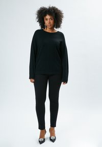 Pullover nero oversize con maniche ampie, abbinato a leggings neri aderenti. Il modello indossa tacchi neri con dettagli decorativi in argento.