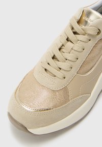 Beige sneakers med semsket og glinsende metallisk finish, med lette snørebånd, rund tå og en teksturert overflate foran.