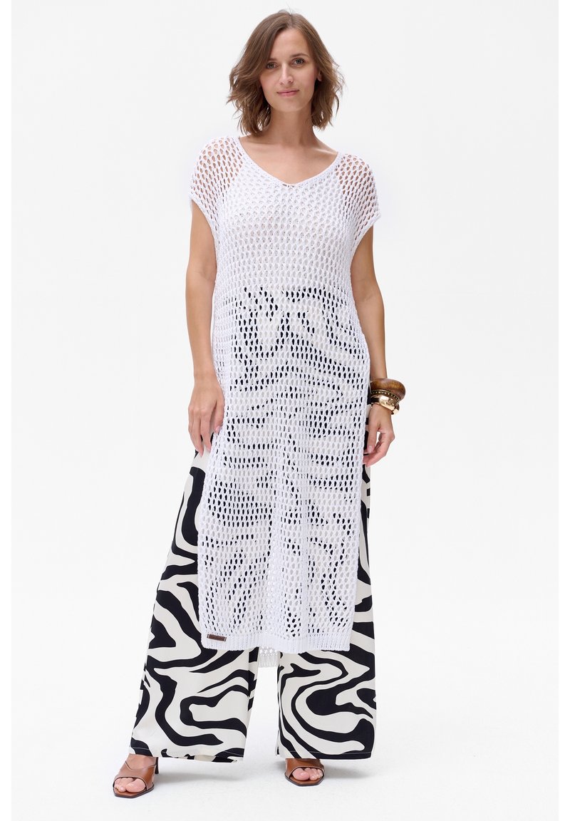 Witte gehaakte cover-up met korte mouwen, met een open brei-design. Gecombineerd met zwart-witte wijde broek met zebrapatroon.