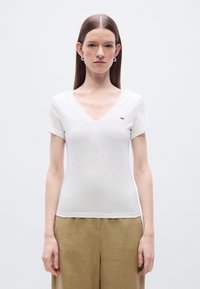 Λευκό βαμβακερό μπλουζάκι με κοντά μανίκια και V-λαιμόκοψη, με ένα μικρό πολύχρωμο λογότυπο στο στήθος. Απλός και εφαρμοστός σχεδιασμός.