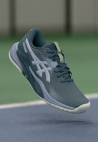 Mørk teal atletisk sko med åndbart mesh-overdel, tekstureret overflade, hvide accenter og perforeringer, med en polstret sål og snørebånd.