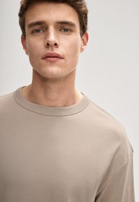 Jasno beżowy t-shirt z zaokrąglonym dekoltem, wykonany z miękkiej tkaniny. Posiada krótkie rękawy i luźny krój, bez widocznych wzorów czy zdobień.