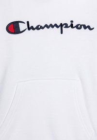 Biela mikina s predným vreckom; vyšívané logo "Champion" v čiernej farbe s červeným akcentom na ľavej strane. Jemná textúra látky.