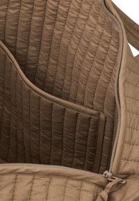 Pruunist tikandiga kanga kotist interjöör, millel on tekstuuriline viimistlus, lukuga sulgemine ja küljetasku korraldamiseks.