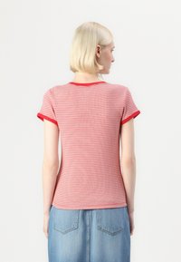 Rød og hvit stripete T-skjorte med korte ermer og rød kant, med en tettsittende design og myk ribbet tekstur, kombinert med denim.