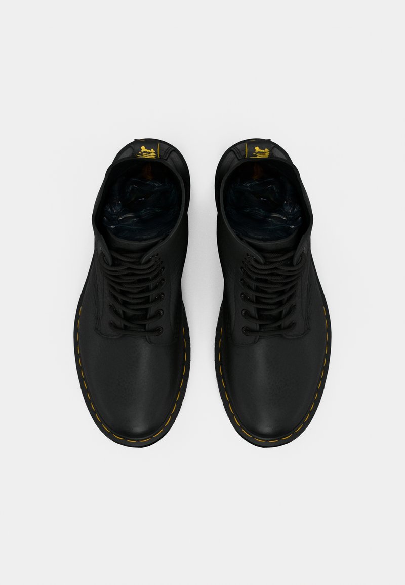 Un par de botas de cuero negro con cordones, con costuras amarillas y tiradores con la marca, vistas desde arriba sobre un fondo blanco.