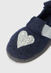 Pantofole in feltro blu con un design a cuore glitterato argento, cinturino elastico e suola in gomma nera texture.