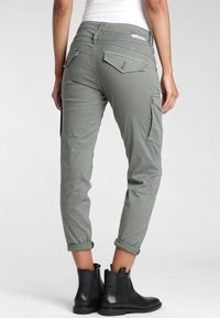 Olivgrön cargo-byxor med en tapered fit, uppvikta nedre kanter och två fickor med lock på baksidan. Matchas med svarta ankelstövlar.