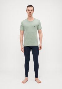 Ljusgrön t-shirt med kort ärm och en svart logotyp, samt mörkblå leggings. Stoftet verkar slätt och elastiskt, och sitter tätt mot kroppen.