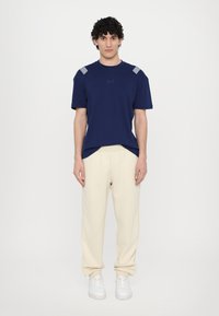 T-shirt en coton bleu marine avec des accents rayés sur les épaules, associé à un pantalon de survêtement crème et des baskets blanches.