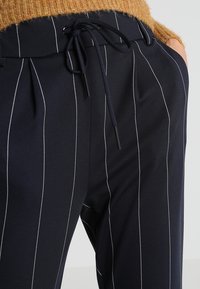 Navy trousers with white pinstripes, featuring a drawstring waistband and pockets. The fabric appears smooth and lightweight.