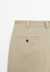 Pantaloni beige su misura con una texture liscia, dotati di una tasca posteriore chiusa da un bottone nero e passanti per cintura in vita.