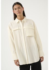 Witte gestructureerde oversized shirt met een knoopsluiting aan de voorkant, twee borstzakken en lange mouwen, met een subtiel ribpatroon.