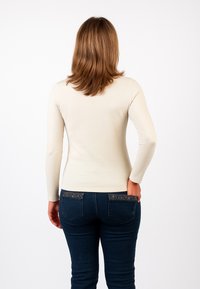Top a maniche lunghe color crema realizzato in tessuto morbido, abbinato a jeans blu scuro con tasche posteriori decorate.