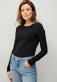 Sort langærmet t-shirt med rund halsudskæring, lavet af glat stof, kombineret med lys blå højtaljede denimjeans.