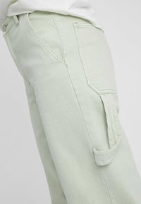 Pantalon cargo en coton vert clair, doté d'une poche latérale, de détails cousus et d'une finition légèrement texturée.