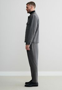 Grau strukturiertes Anzug mit einer geknöpften Jacke und einer Brusttasche, kombiniert mit passenden schmalen Hosen und schwarzen Slippern.