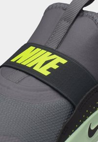 Κοντινό πλάνο γκρι αθλητικού παπουτσιού Nike με κίτρινο λογότυπο Nike σε μαύρο λουράκι πάνω από το πάνω μέρος του παπουτσιού.