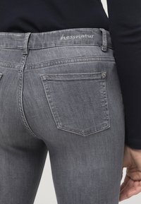 Grå denimjeans med en kroppsnäv silhuett. Har bakfickor och en slät yta. Midjebandet har märket "hessnatur" broderat.