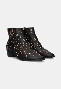 Botines de cuero negro con puntas afiladas y un tacón bajo en bloque. Decorados con tachuelas doradas y acentos de estrellas, con una cremallera lateral.