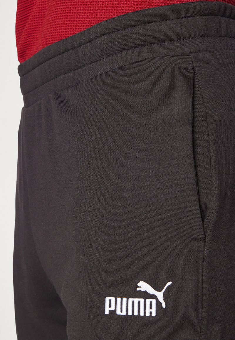 Pantalones de chándal negros con bolsillos laterales, textura de tela suave, cinturilla elástica y logo blanco de Puma en la parte inferior izquierda.
