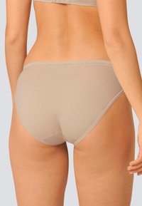 Slip in cotone beige con texture liscia, caratterizzato da un sottile elastico in vita e delicate rifiniture in pizzo lungo i bordi. Design a copertura standard.