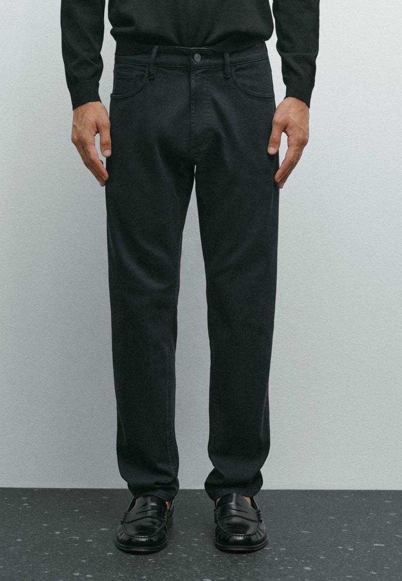 Pantaloni in denim nero con vestibilità dritta, tasche frontali e chiusura con un solo bottone. Texture liscia e design minimale.