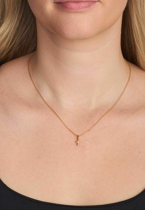 Kultainen ketjukaulakoru, jossa on pieni ristiriipus, herkkä muotoilu, hienot lenkit ja sileä viimeistely, pidetty paljaalla kaulalla.