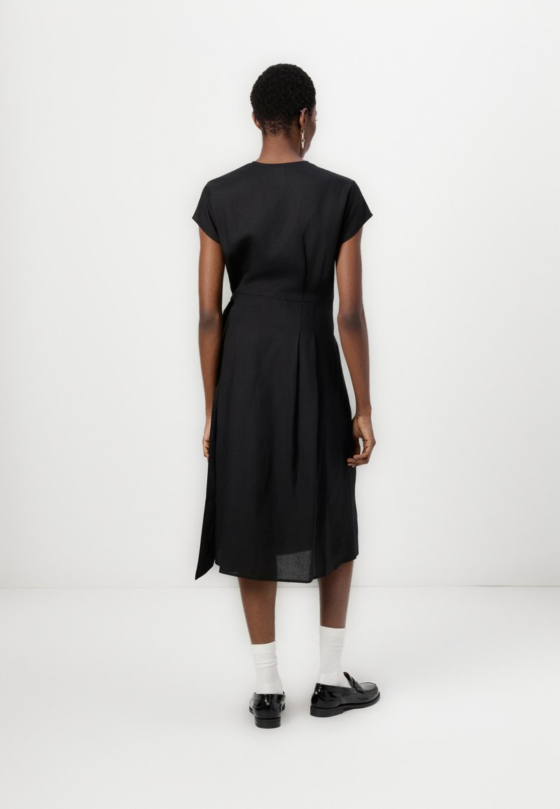 Czarna-midi sukienka, krótkie rękawy typu cap, luźny krój, boczne rozcięcia, lekki materiał. Noszona z czarnymi butami i białymi skarpetkami.