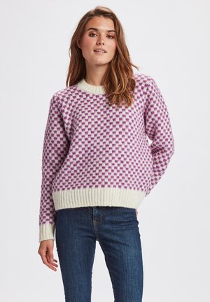 Stickad tröja med rutig mönster i lila och vitt, med ribbad rund halsringning och nederkant, matchad med mörkblå jeans.