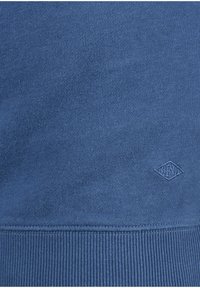 Niebieska bluza z prążkowanymi mankietami i wykończeniem na dole, wykonana z teksturowanej tkaniny. Haftowane logo w dopasowanym kolorze na dole.