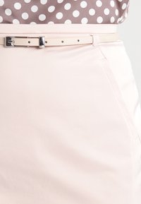 Helle rosa Rock aus glattem Stoff, mit slim Fit, einem dünnen Gürtel mit einer silbernen Schnalle und dezenten Seitentaschen.